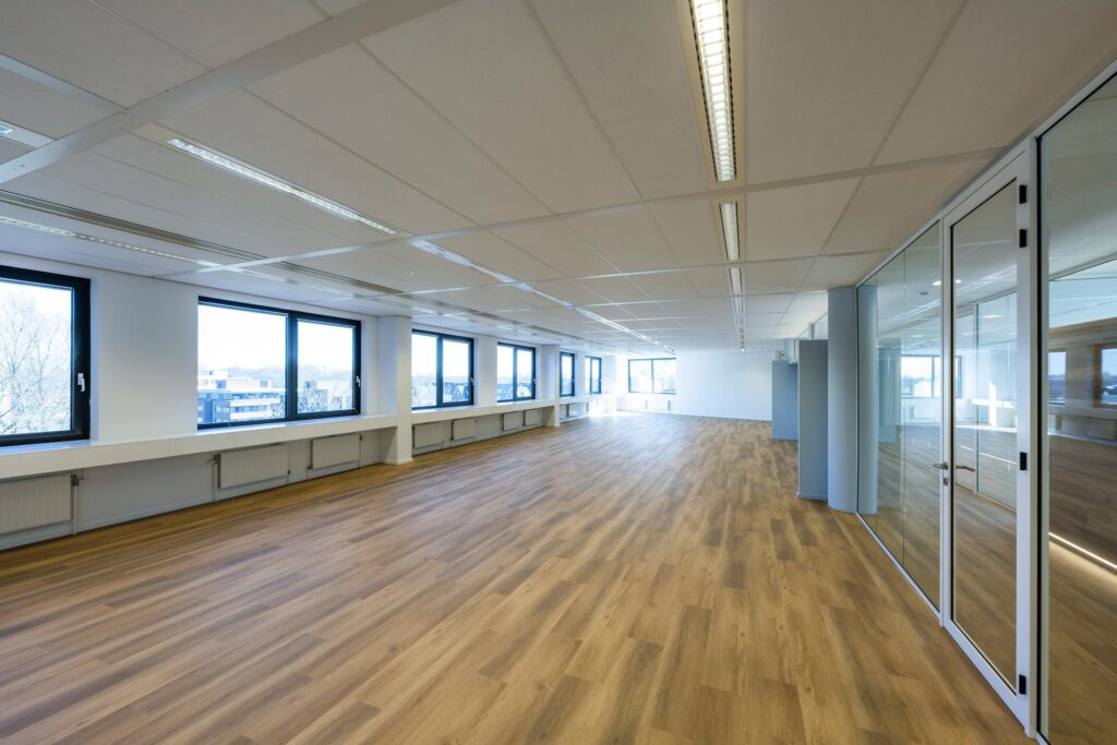 Licht en modern kantoorinterieur aan de Prof. W.H. Keesomlaan met houten vloer, grote ramen en glazen scheidingswanden.